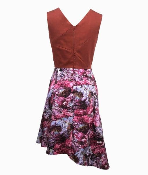 Back view of a burnt orange top above the waist with architectural lines and a wookey hole cave print skirt that is asymmetrically longer on the left side.