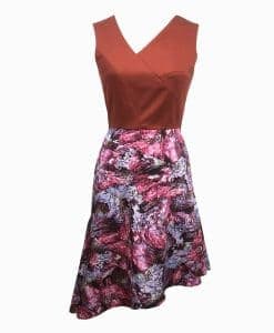 Front view of a burnt orange top above the waist with architectural lines and a wookey hole cave print skirt that is asymmetrically longer on the left side.